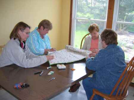 Friends help by hand-sewing the binding on the quilt